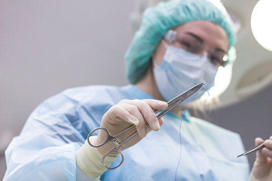 Surgeon resuscitator, close-up cuts the thread during surgery, suture the patient. The doctor in the operating room holds a metal tool closeup