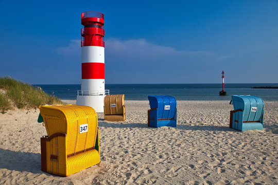 colorful beach chairs and red and white lighthouse on düne with empty beach