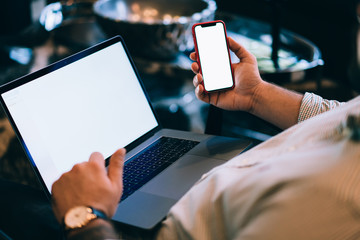 Back Close up of caucasian young man holding blank display mobile phone in hands, verification of banking data, shopping online on laptop computer and cellphone with mock up screen for web advertising