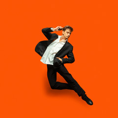 Man in casual office style clothes jumping and dancing isolated on bright orange background....