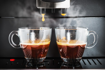 two cups of freshly brewed coffee in the coffee machine. Shallow depth of field, focus on coffee drop