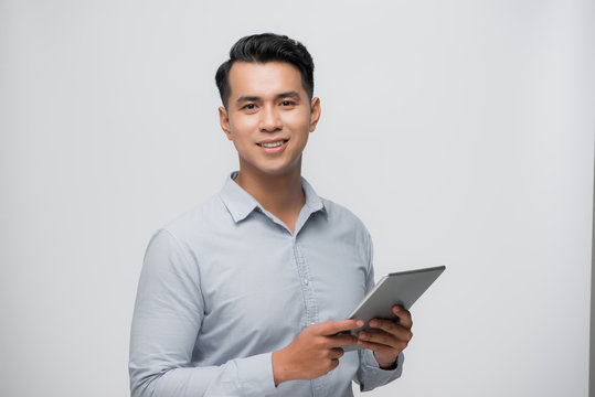 Photo of young happy man standing over white background using tablet computer.