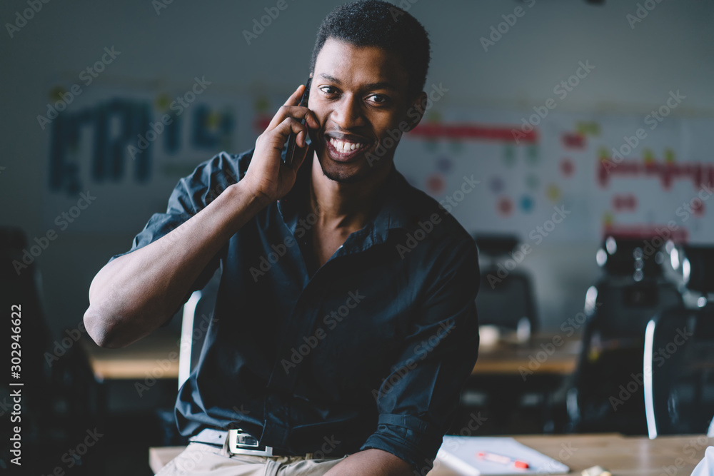Poster portrait of successful cheerful male entrepreneur looking at camera and making positive smartphone c