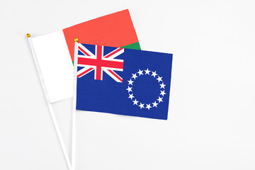 Fototapeta premium Cook Islands and Madagascar stick flags on white background. High quality fabric, miniature national flag. Peaceful global concept.White floor for copy space.