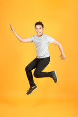 Fototapeta na wymiar Full length portrait of an excited young man in white t-shirt jumping while celebrating success isolated over orange background