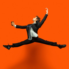 Fototapeta na wymiar Man in casual office style clothes jumping and dancing isolated on bright orange background. Business, start-up, open-space, inspiration concept. Flexible ballet dance. Hurrying up, drinking coffee.