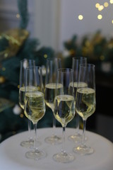 Six glasses for champagne and golden Christmas balls against a background of blurred golden lights. Celebrating New Year, Christmas or Birthday with glasses of champagne at party