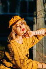 Beautiful girl in a yellow beret poses near the grid. Reflection of stripes on face at sunset