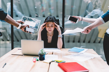 Young disappointed woman feeling headache from deadline surrounded by colleagues at workplace, multi-purpose female employee,tired of work and exhausted, stress in office. Overworked female in confuse