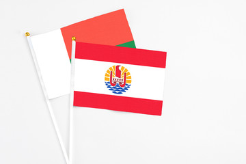 French Polynesia and Madagascar stick flags on white background. High quality fabric, miniature national flag. Peaceful global concept.White floor for copy space.