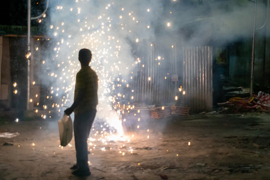 Image of young man lighting up fire crackers at night,event of Kali Puja, a Hindu Indian festival - for spiritual celebration of light over eternal darkness.The fireworks create air pollution.