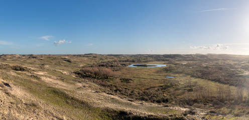 Panoramic view from a high dune top on a valley with a dune lake and the contours of a village on the horizon