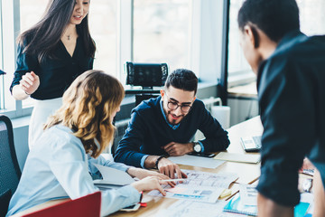 Diverse young people discussing strategy and collaborating on building sketch having brainstorming meeting.Multicultural male and female colleagues cooperating on architectural blueprint in office