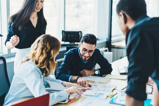 Diverse young people discussing strategy and collaborating on building sketch having brainstorming meeting.Multicultural male and female colleagues cooperating on architectural blueprint in office
