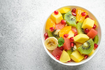 Bowl with homemade fresh fruit salad: mango, grapefruit, pomegranate, kiwi, banana on a light background top view copy space.