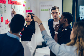Group of professional male and female multicultural employees in formal wear pointing on glued...
