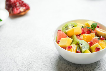 Bowl with homemade fresh fruit salad: mango, grapefruit, pomegranate, kiwi, banana on a light background top view copy space.