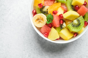 Bowl with homemade fresh fruit salad: mango, grapefruit, pomegranate, kiwi, banana on a light background top view copy space.
