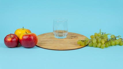 Glass of juice with fresh grape and apples on blue background.