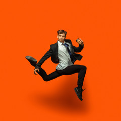 Fototapeta na wymiar Man in casual office style clothes jumping and dancing isolated on bright orange background. Business, start-up, open-space, inspiration concept. Flexible ballet dance. Hurrying up, drinking coffee.