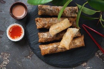 Stone slate tray with vietnamese nems and dipping sauces, top view over brown stone surface, close-up