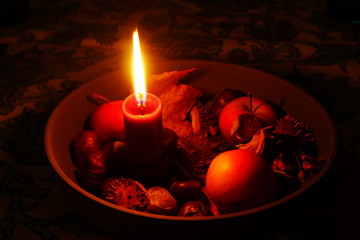 Rote brennende Kerze in einer Schale mit Kastanien und Laub