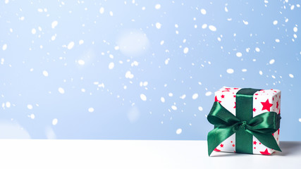Christmas gift box with green ribbon bow in snow on blue background. Christmas, New Year, winter holidays concept