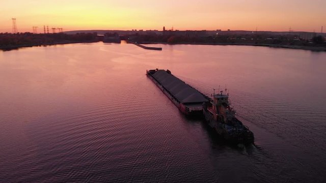 aerial view. Sunset over the water channel. The cargo barge goes towards the locks. A bulk carrier transports a large volume of crushed stone for construction.