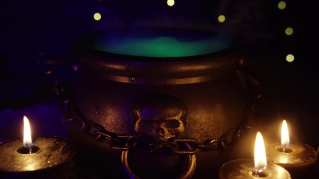 Halloween Bubbling smoking witch's cauldron with neon glowing vials and crystal ball in foreground. A hand empties poison into the pot. Witch and wizard concepts. RED Camera, Slow motion.