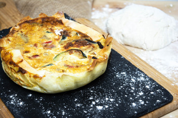 Vegetable quiche on wooden background with flour dough in the background. Typical dish of French cuisine. Vegetarian Food. Homemade food prepared