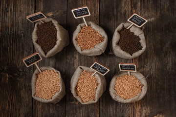 Grain of wheat, rye and barley in small burlap sacks on a wooden background. Name of the variety of grains on a wooden plate frame. Rustic, farm concept. Copy space. Top view