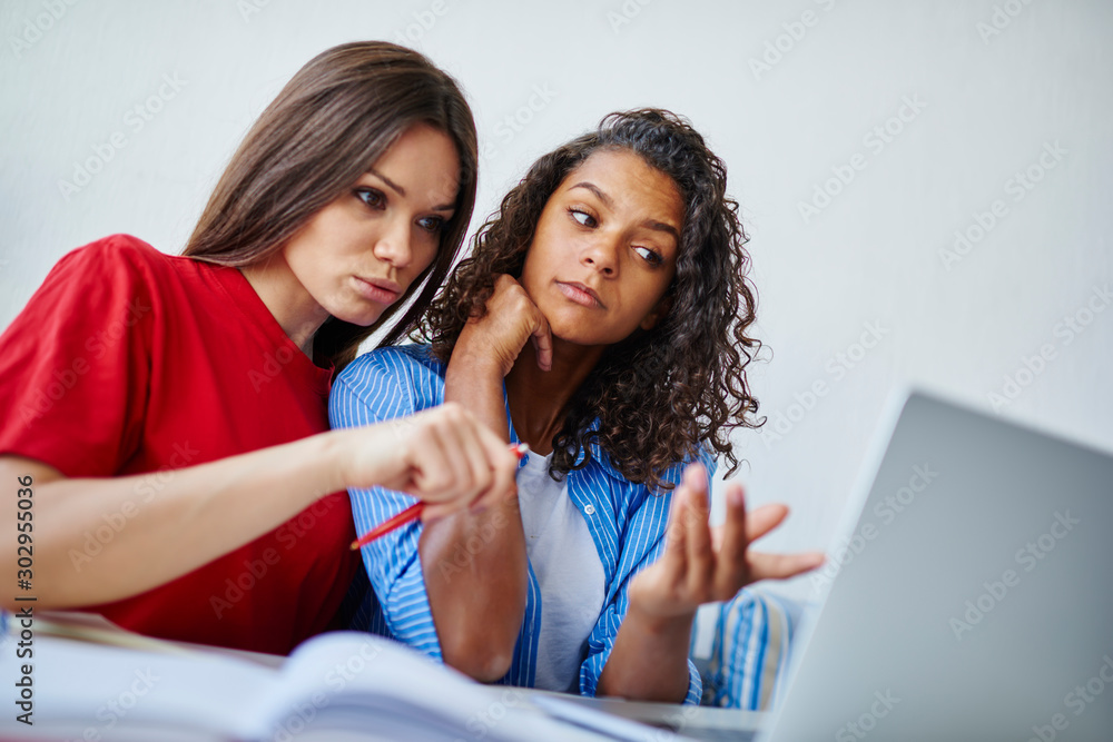 Poster clever multiracial female students discussing ideas for coursework project reading information from 