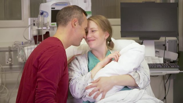 Medium shot of new parents fawning over their newborn baby in the hospital.