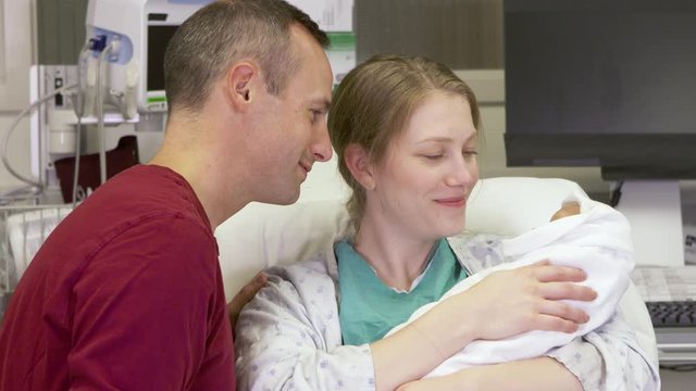 Close-up of new parents lovingly admiring and holding their newborn baby for the first time after giving birth in the hospital.