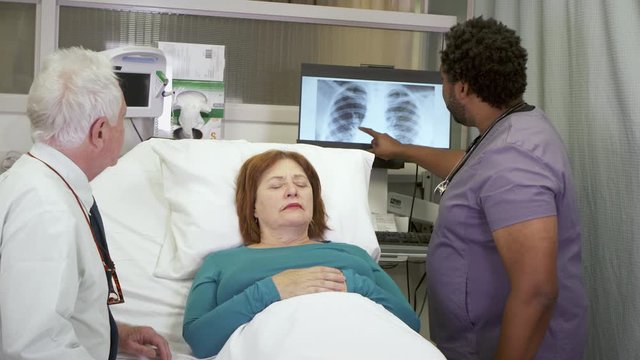 A male nurse discusses x-rays with the husband as the wife is unconscious in a hospital bed.