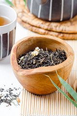 Green tea in bowl with cup of tea and black teapot on white  table with bamboo leaves .