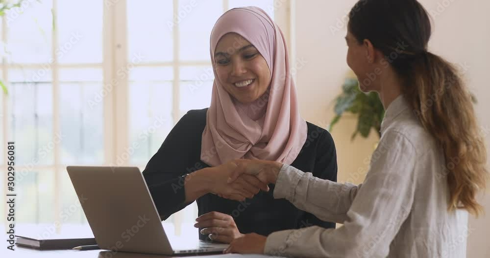 Sticker happy asian muslim manager handshaking caucasian female client at meeting