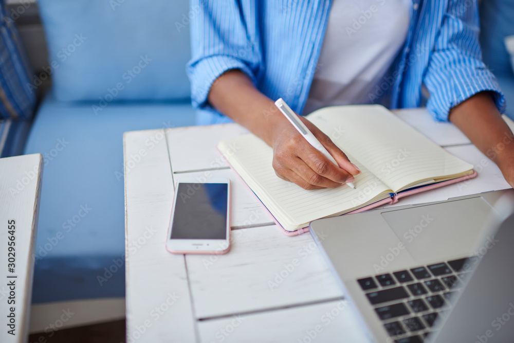 Poster cropped image of african american female holding pen writing in notepad with blank pages doing homew