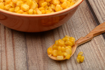 Sweet corn kernels in a plate and on a wooden spoon on a wooden table. Fitness diet. Healthy diet. For a sweet treat. Close up.