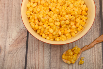 Sweet corn kernels in a plate and on a wooden spoon on a wooden table. Fitness diet. Healthy diet. For a sweet treat.