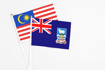 Fototapeta premium Falkland Islands and Malaysia stick flags on white background. High quality fabric, miniature national flag. Peaceful global concept.White floor for copy space.