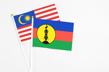New Caledonia and Malaysia stick flags on white background. High quality fabric, miniature national flag. Peaceful global concept.White floor for copy space.