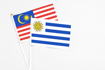 Uruguay and Malaysia stick flags on white background. High quality fabric, miniature national flag. Peaceful global concept.White floor for copy space.