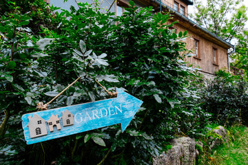 advertisement plate tablet sign countryard patio index direction pointer branches green yellow blue house evergreen