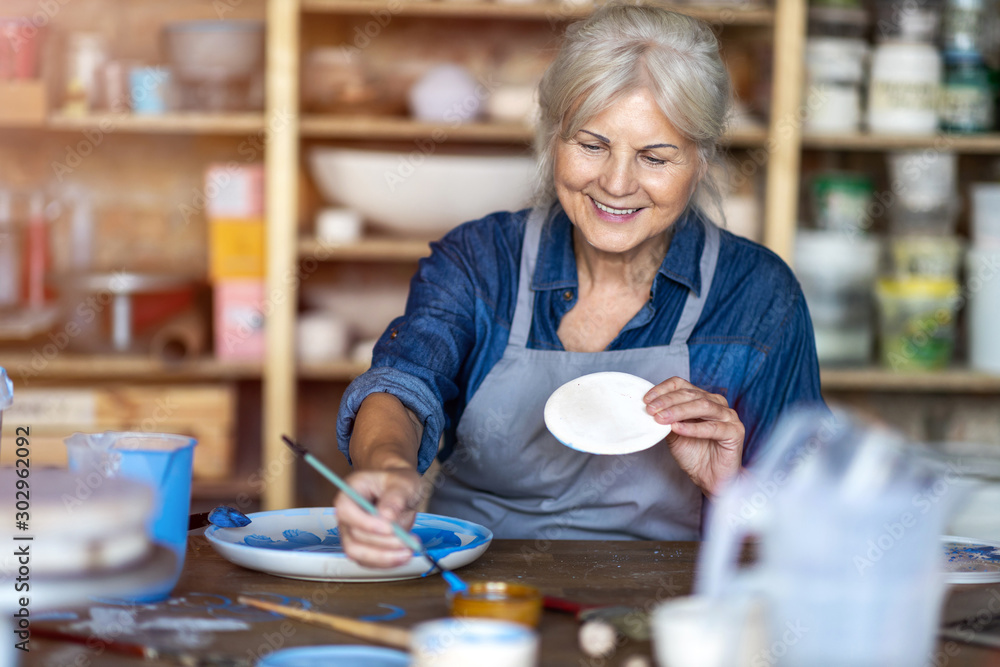 Wall mural mature craftswoman painting a plate made of clay in art studio