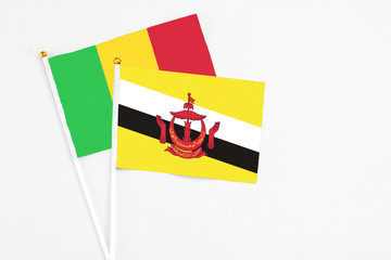 Brunei and Mali stick flags on white background. High quality fabric, miniature national flag. Peaceful global concept.White floor for copy space.