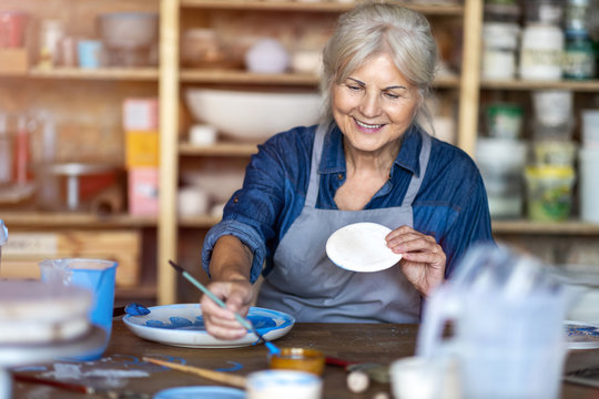 Mature craftswoman painting a plate made of clay in art studio