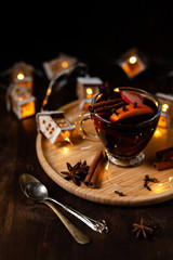 Christmas delicious hot mulled wine with orange, apple, cinnamon, clove, cardamom and anise on wooden plate. Warm beverage for cold winter days. Brights lights create festive mood. Dark background