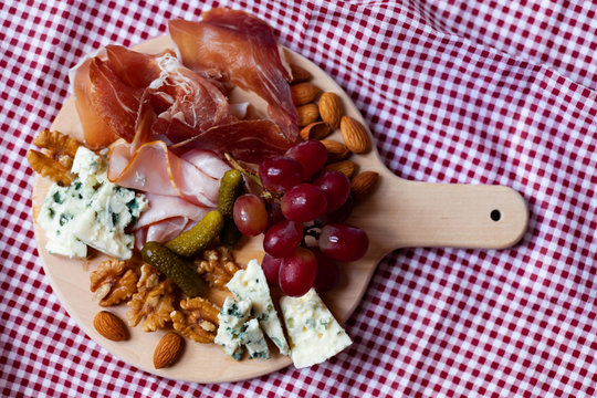 Delicious aperetif for evening home party: wooden borad with french blue cheese, bacon, walnut and almond, italian sweet grapes. Closeup, top view