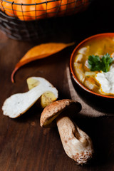 Delicious hot porcini soup with cream in black clay pan. Tasty seasonal autumn meal. Fresh mashrooms illustrate ingredients. Concept of homemade food. Closeup, dark wooden background